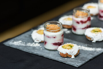 little bun with a dessert in a glass cup, with Jello, yogurt and topping served on a ceramic plank. Mini desserts