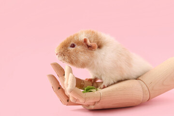 Funny Guinea pig with lettuce and wooden hand on pink background