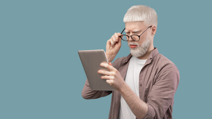 Shocked albino man staring at tablet screen and reading news over turquoise background, panorama with empty space.