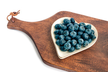 Fresh juicy delicious blueberries lie on a white original plate in the form of a heart, a kitchen...