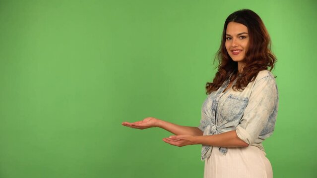 A young beautiful Caucasian woman presents something to the camera with a smile - green screen background