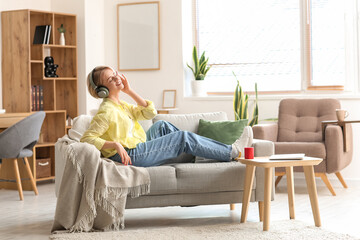 Young woman sitting on sofa and listening to music in light room