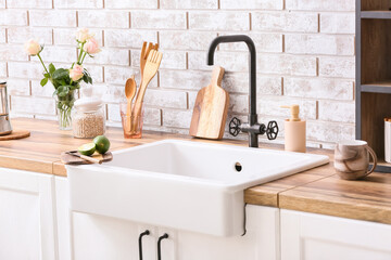 Fototapeta na wymiar Cutting board with lime and knife on ceramic sink near light brick wall