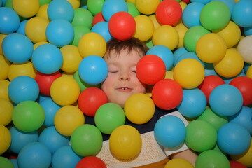 Fototapeta na wymiar A cheerful boy is playing in the playroom in the pool with balls of different colors