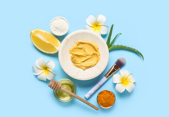 Composition with turmeric mask, powder, lemon and makeup brush on blue background