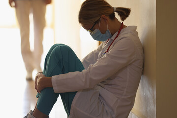 A female doctor is sitting on the floor in the hallway, close-up