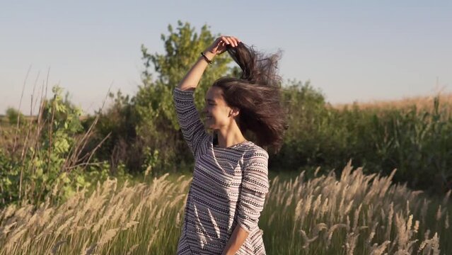 The wind blows the hair and dress of a beautiful young girl standing in the field. Slow motion.