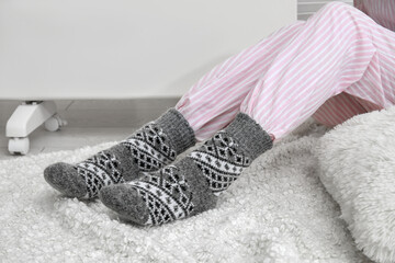 Woman in warm socks sitting near electric heater at home. Concept of heating season