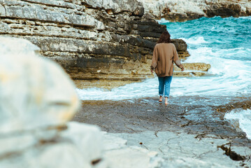 woman walking by rocky sea beach at sunny windy day. summer vacation