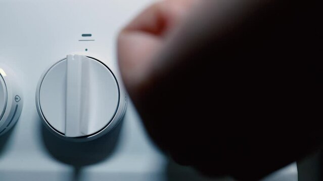 Female hand twisting the handle on modern gas stove or oven at home.