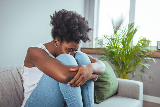 Side view young woman looking away at window sitting on couch at home. Frustrated confused female feels unhappy problem in personal life quarrel break up with boyfriend or unexpected pregnancy concept