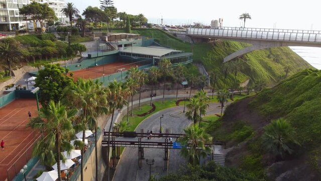 Drone footage of "Bajada Balta" a street in Miraflores, Peru. Filmed flying forwards and slowly turning right to reveal a bridge and the beach and sun behind it.