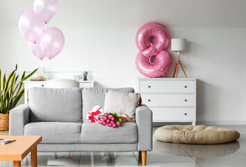 Bouquet of tulip flowers with gift on sofa in interior of room