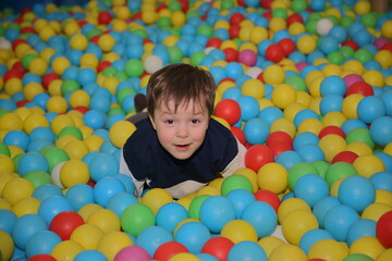 Fototapeta na wymiar A cheerful boy is playing in the playroom in the pool with balls of different colors