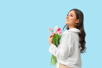 Obraz na płótnie Canvas Fashionable woman with creative makeup holding bouquet of tulips on blue background. International Women's Day