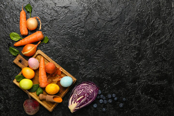 Wooden board with Easter eggs and natural dyes on dark background