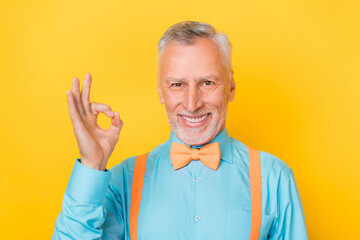Photo of old grey hairdo man show okey wear teal shirt suspenders bow tie isolated on yellow color background