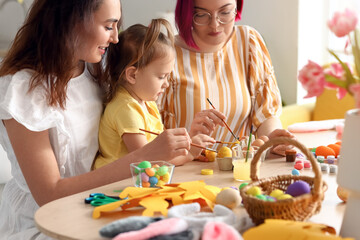 Young lesbian couple with little daughter during painting of Easter eggs in kitchen