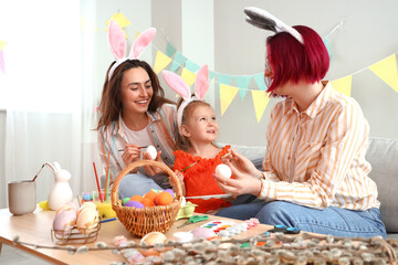 Young lesbian couple with little daughter painting Easter eggs at home