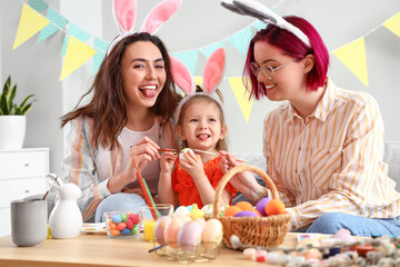 Young lesbian couple with little daughter having fun while painting Easter eggs at home