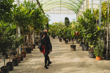 Chica joven guapa morena con mascarilla por covid 19 comprando en un vivero plantas y arboles