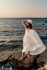 Fototapeta na wymiar A woman in a white dress and hat is standing on the beach enjoying the sea. Happy summer holidays.