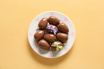Plate with chocolate Easter eggs and bows on color background