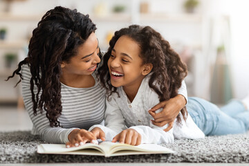 Joyful black girl reading book with her mom