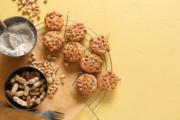 Cooling rack with tasty peanut cookies and flour on yellow background