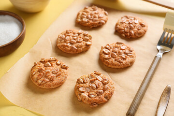 Parchment paper with tasty peanut cookies on yellow background