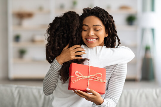 Cheerful black lady with gift box hugging her daughter