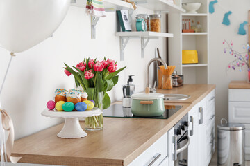 Stand with Easter cakes and eggs on counter in kitchen decorated for holiday