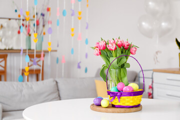 Basket with Easter eggs, vase and tulips on dining table in kitchen