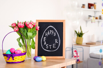 Chalkboard with text HAPPY EASTER, eggs and tulips on table in kitchen