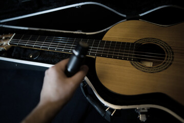 A black microphone in his hand against the background of a classical guitar in a black trunk on a dark background. Dynamic microphone and flamenco guitar