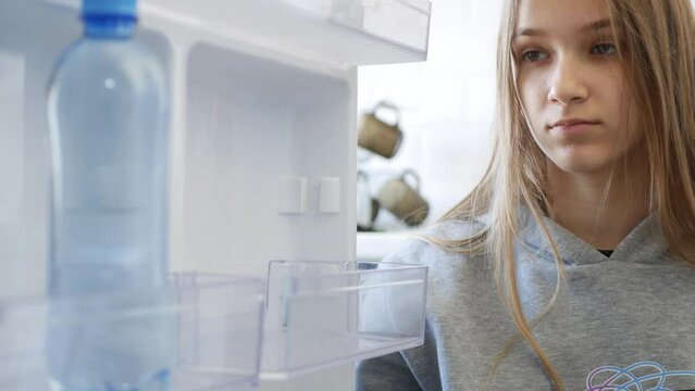 Child Opening Fridge, Kid Took a Bottle of Water in Refrigerator, Sad Girl Looking Food in Poor Empty Freezer Poverty in Kitchen