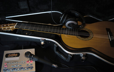 Fototapeta na wymiar Musical accessories. Street musician's instruments. A guitar in a black trunk on a dark background with a microphone, a drum machine turned on and headphones.