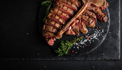 Barbecue dry aged wagyu porterhouse beef steak sliced with large fillet piece with hot chili as closeup on a modern design black cast iron tray