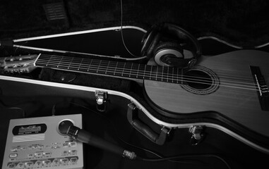 Black and white photo with a guitar in a case. Headphones microphone and drum machine. Musical accessories. Classical or flamenco guitar in a black case