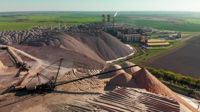 Extraction of minerals from earth. Working giant earthmower with conveyour belt, Soligorsk potash factory in the background. Aerial view on a sunny day, blue sky. 
