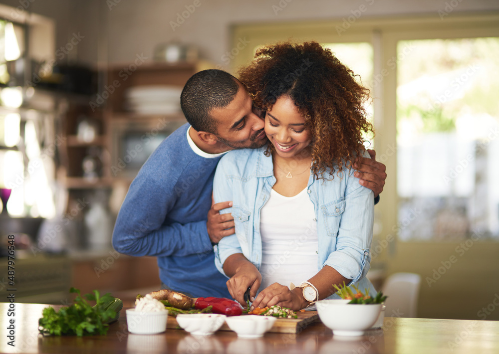 Poster The healthy marriage is a happy marriage. Shot of a young man kissing his wife while she prepares a healthy meal at home.