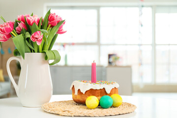 Fototapeta na wymiar Easter cake, burning candle, eggs and vase with tulips on dining table in kitchen