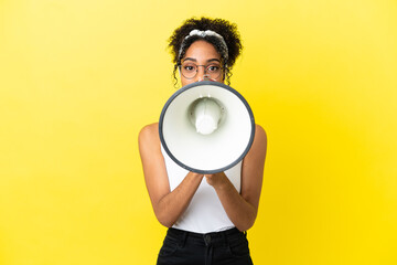 Young african american woman isolated on yellow background shouting through a megaphone to announce something