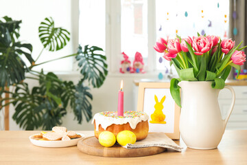 Fototapeta na wymiar Easter cake, candle, eggs, cookies, picture and vase with tulips on counter in kitchen