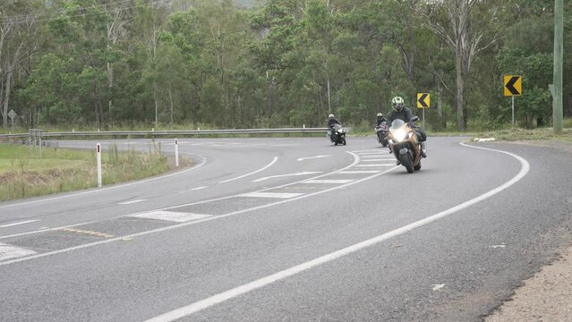 Group of motorcyclists ride around a bitumen corner and pass camera. Filmed in regional Queensland, Australia.