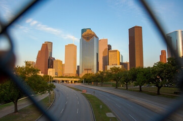 Downtown Houston skyscraper skyline at twilight with no traffic on freeway in forefront. POV through chainlink fence.
