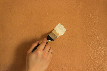 Man's hand holds paint brush and paints the brown wall in white color. Repair and renovation of the...