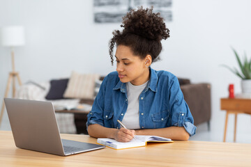 Online education concept. Beautiful concentrated African American woman freelancer working from home. Happy female student using laptop computer, studying, distance learning