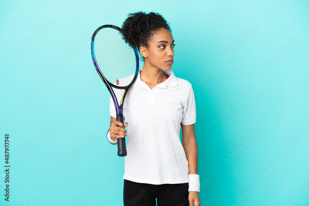 Wall mural Young tennis player woman isolated on blue background looking to the side