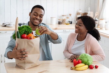 Healthy Eating. Happy african spouses unpacking paper bags with groceries at home